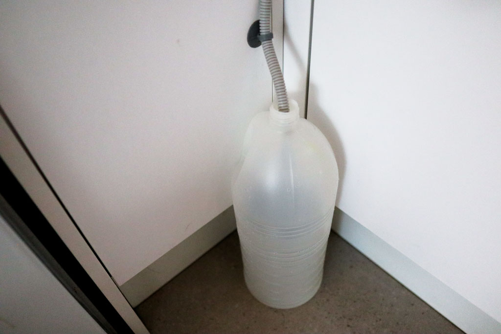 A large plastic jug used as a workaround for draining a baby bottle washer when there is no nearby sink