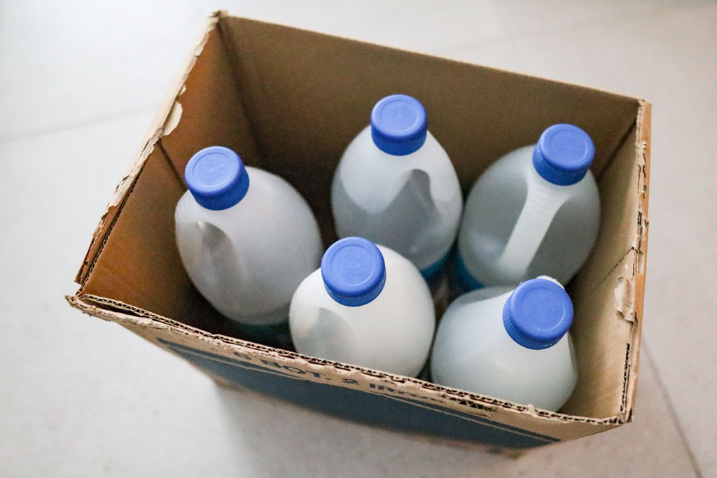 Box of distilled water jugs bought in bulk to prevent hard water scale buildup in a baby bottle washer