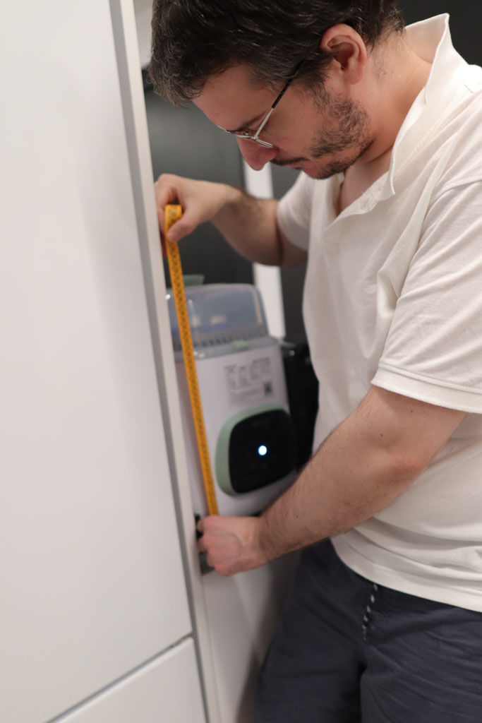 A photo of Dim Nikov, the editor of Dad's Picks, measuring a baby bottle washer with a tape measure for a review.