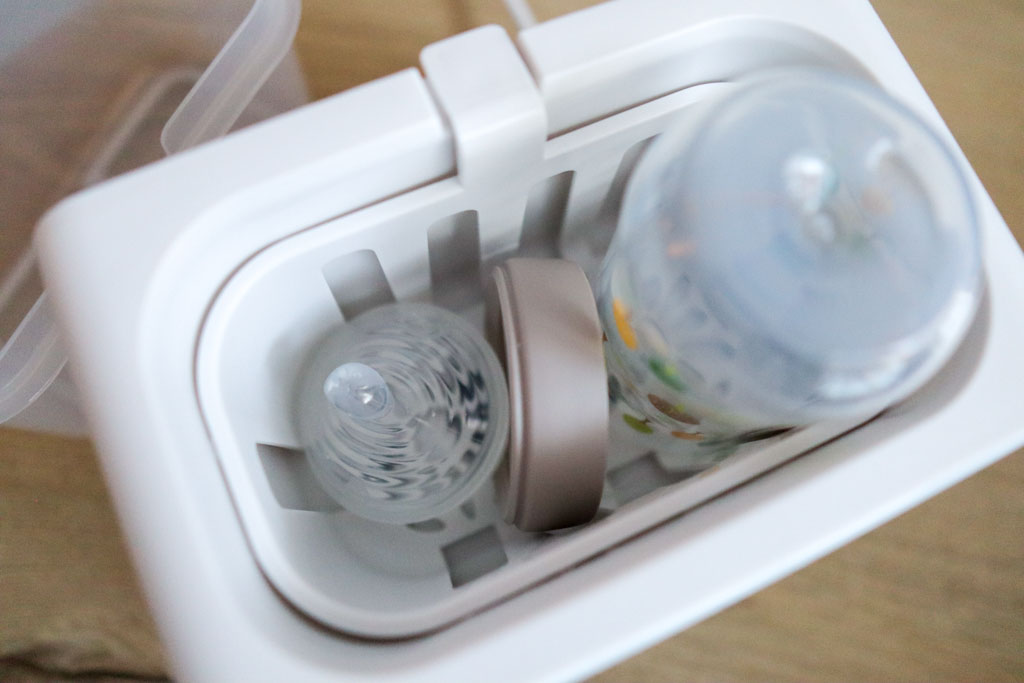 A NUK baby bottle with nipple, ring, and cap placed in the Grownsy 8-in-1 Bottle Warmer's anti-scald basket, ready for sterilization.