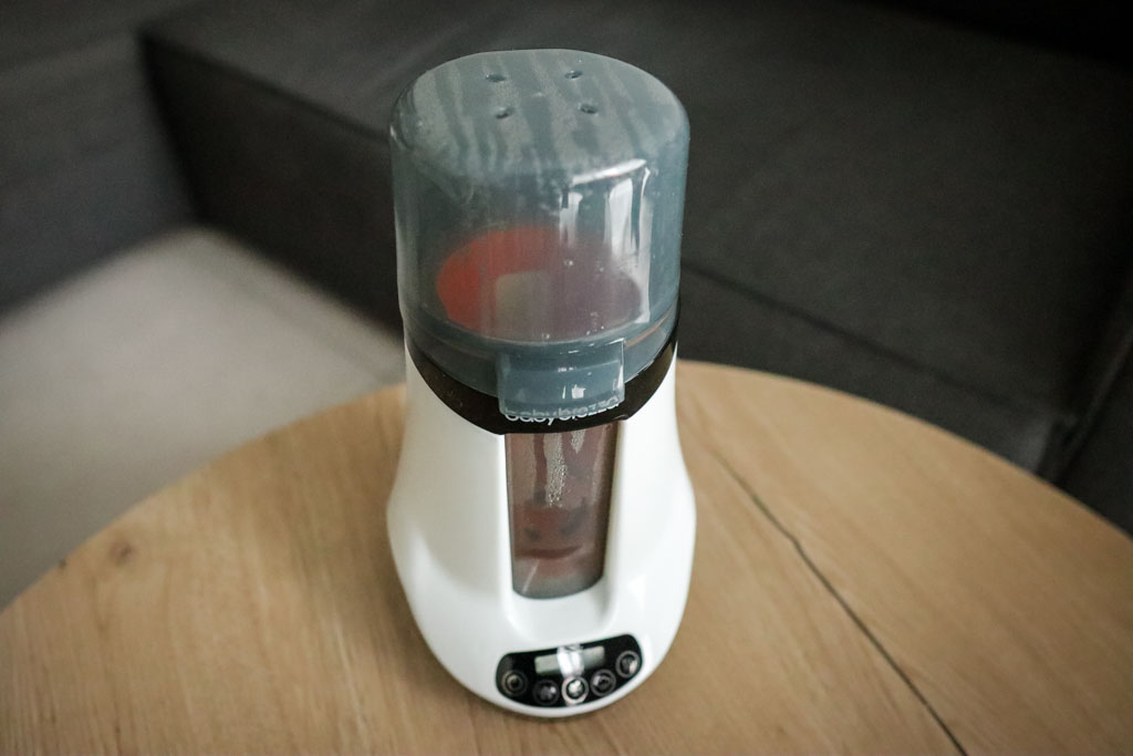 The Baby Brezza Smart Bottle Warmer on a countertop, resembling a compact coffee grinder in its design.